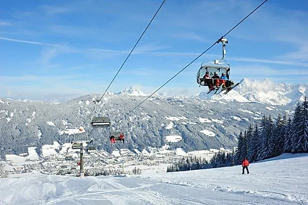 Lyžaři a lanovka na zasněžené sjezdovce v Radstadtu s panoramatickým výhledem na Alpy.