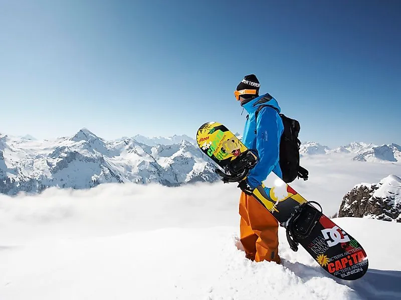 Un snowboarder avec un équipement coloré se tient dans la neige poudreuse devant un panorama alpin près de Stoos