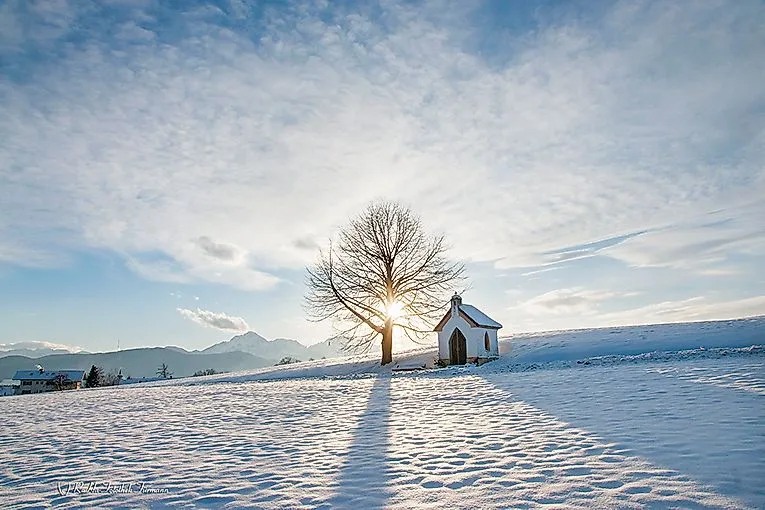 Snowy winter landscape in Anger with chapel, tree and low sun