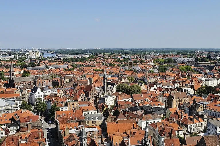 Aerial view of the Zeebrugge district with densely packed red tiled roofs and church towers under a clear blue sky.