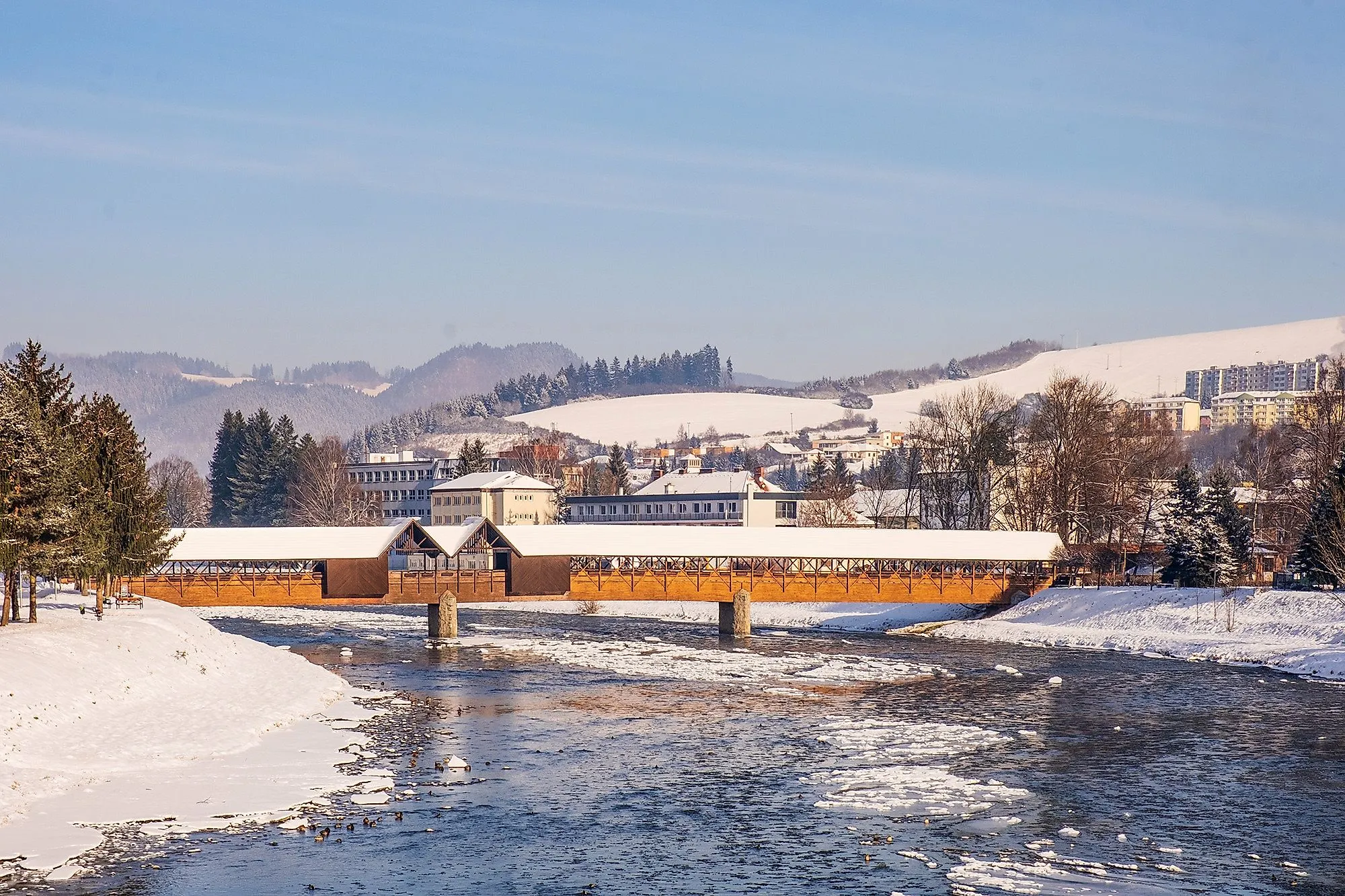 Winter in Dolny Kubin met een overdekte houten brug en besneeuwde heuvels