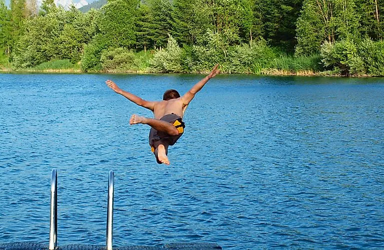 Un niño salta a un lago de aguas cristalinas en Carintia durante sus vacaciones de verano