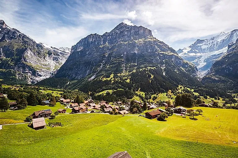 Pohled na idylickou vesničku Grindelwald s tradičními chatami, zasazenou do zelené horské krajiny Bernského pohoří ve Švýcarsku.