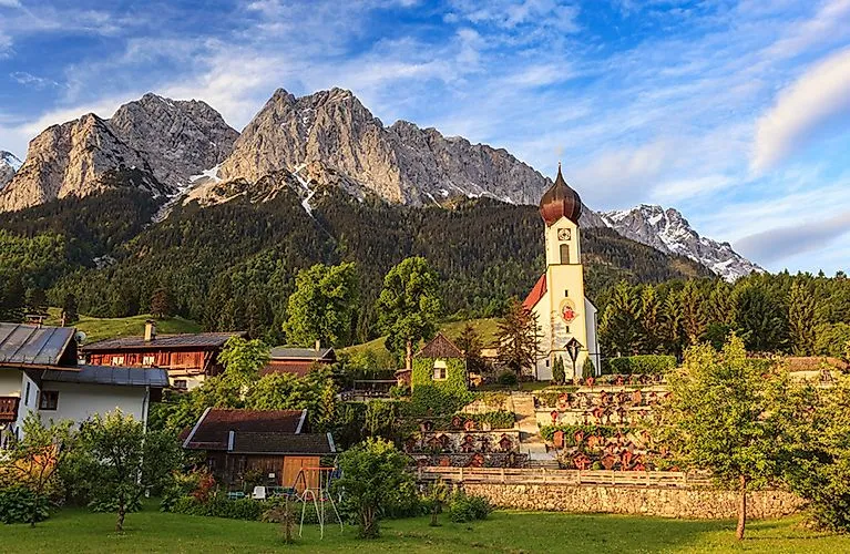 Blick auf Grainau mit Kirche vor der Zugspitze an einem sonnigen Sommertag in den bayerischen Alpen.