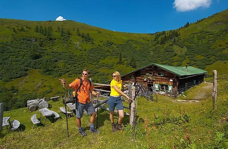 Two hikers in front of an alpine hut in the middle of green meadows and mountains near Bad Hofgastein.