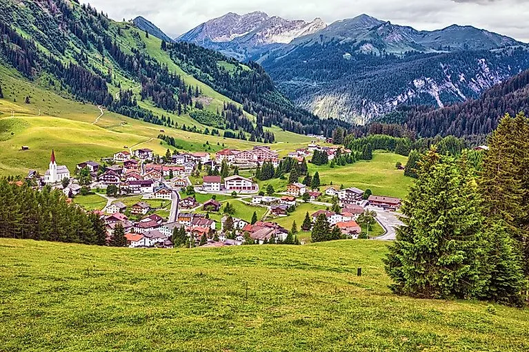 Sommeransicht von Berwang mit traditioneller Tiroler Architektur inmitten saftig grüner Almwiesen und umrahmt von bewaldeten Berghängen.