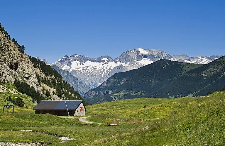 Paisaje veraniego de montaña cerca de Cerler con prados verdes, refugio alpino y vistas de los picos nevados de los Pirineos