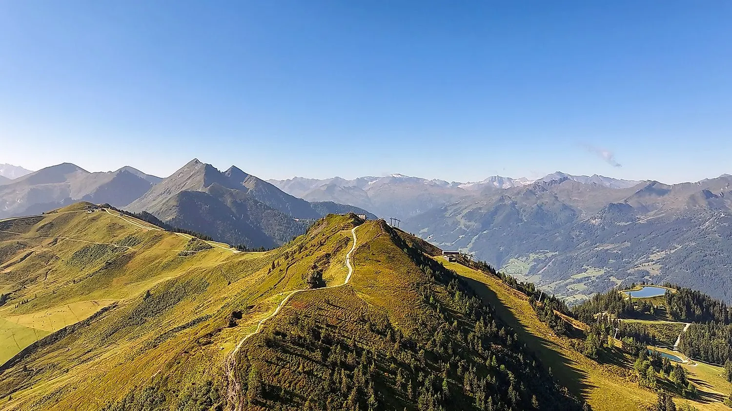 FlyingCam aerial view of the green mountain ridges of Dorfgastein with distant views of the Hohe Tauern in summer.