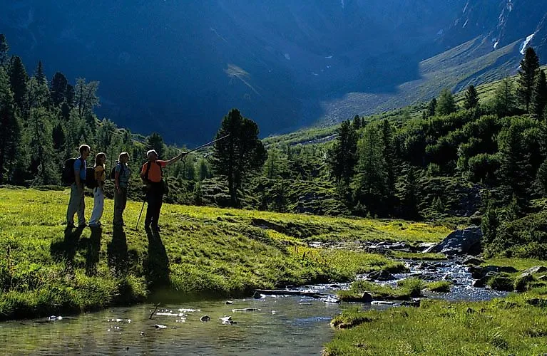 Turistická skupina prozkoumává zelené vysoko položené údolí u Fendels s výhledem na potok a hory