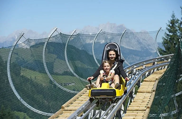 Madre e hijo recorren el paisaje estival de Fieberbrunn en el Timok's Coaster, riendo.