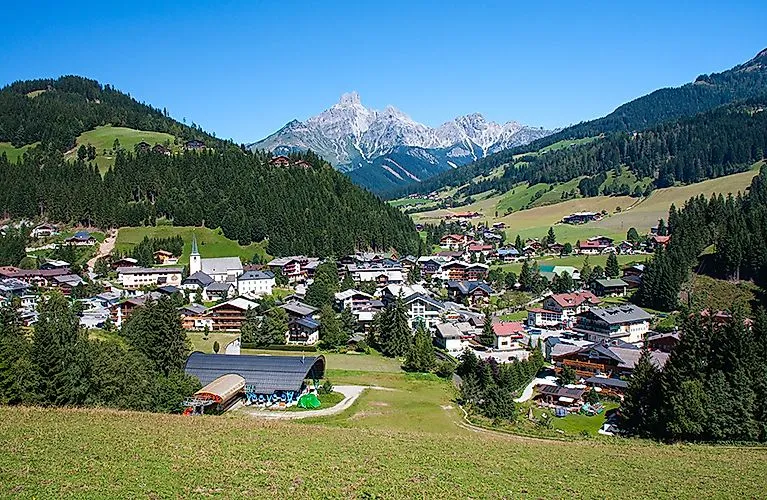 Vista dell'idilliaco villaggio di Filzmoos nelle Alpi salisburghesi, immerso tra verdi colline con il suggestivo massiccio del Dachstein sullo sfondo.