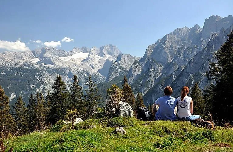 Zwei Wanderer genießen die Aussicht auf die imposanten Berge des Dachsteinmassivs bei Gosau an einem sonnigen Sommertag.