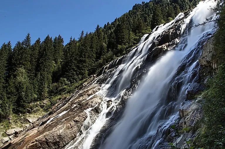 Grawa waterfall in the Stubai Valley, surrounded by dense coniferous forest on a sunny summer's day in Tyrol.