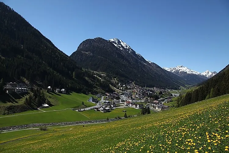 Blick über das sonnige Paznauntal auf den Tiroler Ferienort Ischgl, eingebettet zwischen saftig grünen Berghängen und schneebedeckten Gipfeln.