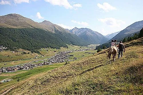 Zwei Reiter auf einem Hügel mit Panoramablick auf das sonnige Tal von Livigno und umliegende Berge