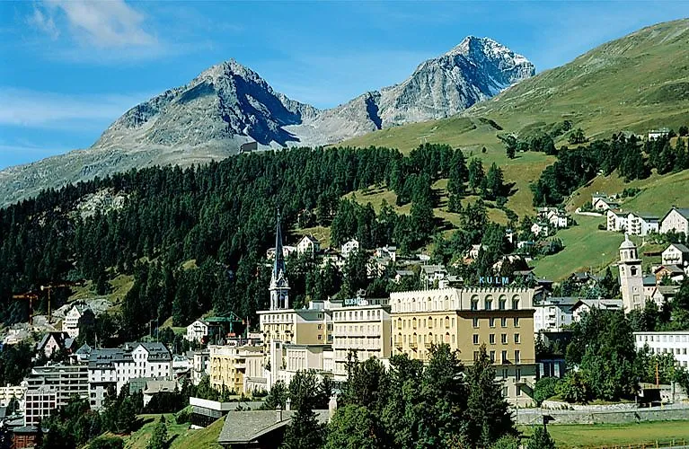 Pohľad na centrálnu časť dediny Svätý Moric s historickým hotelom Kulm a okolitými horami počas slnečného letného dňa.