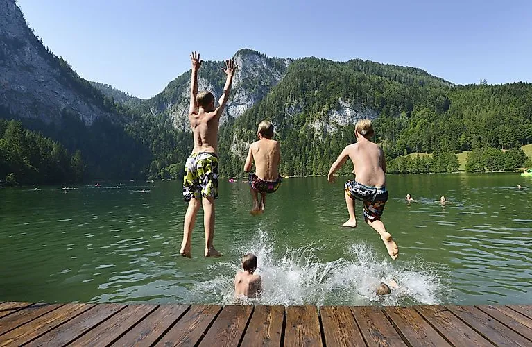 Children laughing as they jump into a clear mountain lake near Windischgarsten on a summer's day.
