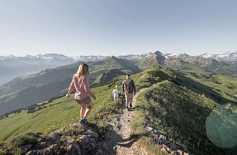 Familie beim Wandern über einen Höhenweg mit herrlichem Ausblick auf das grüne Alpenpanorama rund um Zweisimmen.