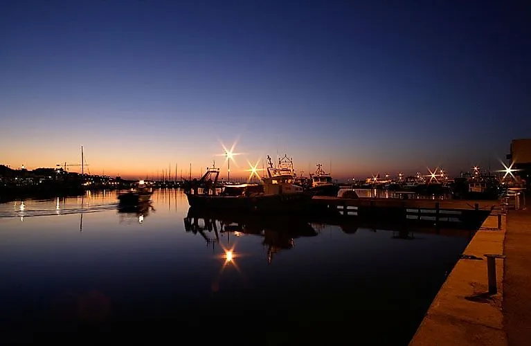 Barcos de pesca en el puerto de Cambrils al amanecer con aguas tranquilas y luces parpadeantes en el cielo matinal