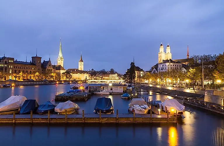 Večerní panoramatický pohled na Curych s osvětleným Starým městem, Fraumünsterem a Grossmünsterem na Curyšském jezeře.