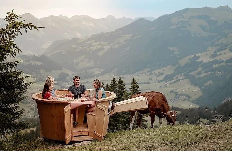 Genießergruppe beim Fondue im Freien mit Panoramablick auf die grünen Berghänge des Rinderbergs in Zweisimmen.