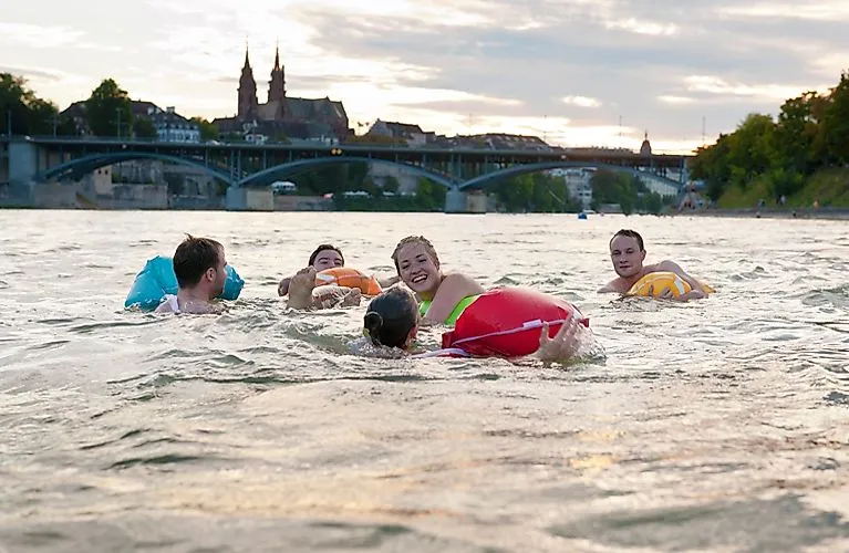Des jeunes gens dérivent à travers Bâle avec des animaux en suspension colorés lors de la populaire natation sur le Rhin, avec la vieille ville en arrière-plan.